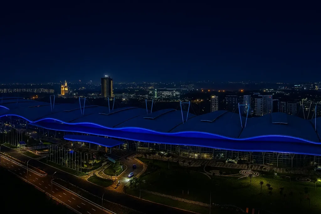 Foto malam hari gedung ICE BSD dengan pencahayaan biru elegan sebagai lokasi utama GIIAS 2025, menampilkan suasana pameran otomotif dari udara.